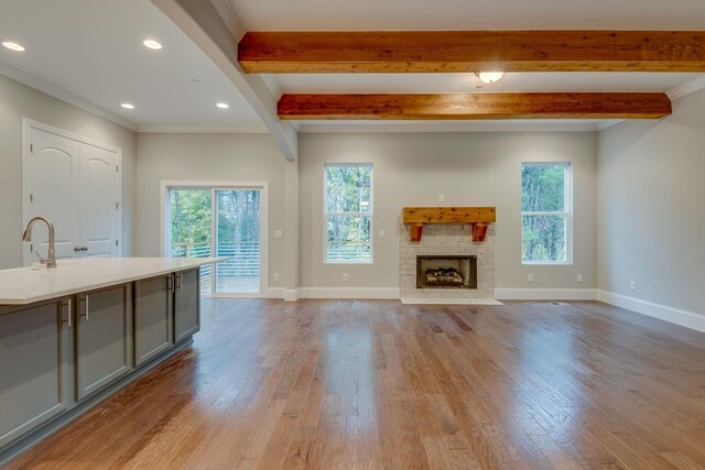 unfurnished living room featuring a fireplace, crown molding, beamed ceiling, and light hardwood / wood-style floors