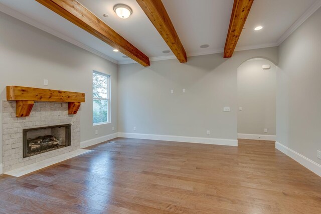 unfurnished living room with beamed ceiling, light wood-type flooring, and crown molding