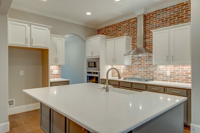 kitchen featuring stainless steel appliances, a kitchen island with sink, wall chimney exhaust hood, and white cabinetry