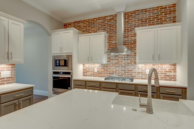 kitchen with appliances with stainless steel finishes, wall chimney range hood, light stone counters, and white cabinets