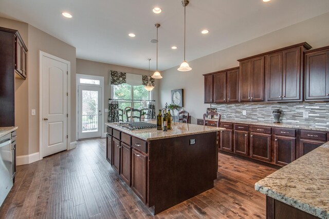 kitchen featuring dark hardwood / wood-style flooring, tasteful backsplash, a center island with sink, pendant lighting, and light stone countertops