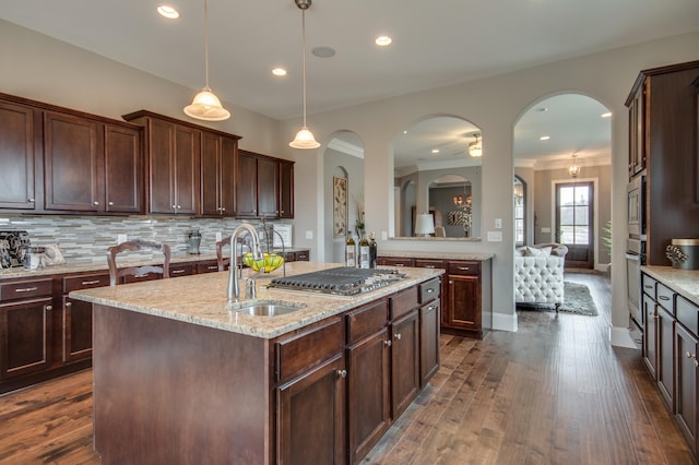 kitchen featuring decorative light fixtures, light stone counters, tasteful backsplash, dark hardwood / wood-style floors, and an island with sink