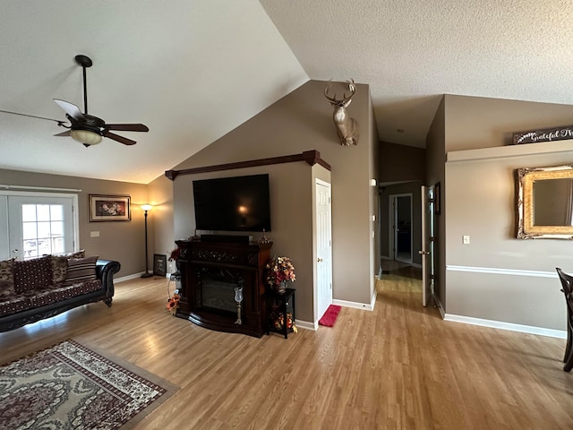 living room with a textured ceiling, lofted ceiling, ceiling fan, and light wood-type flooring