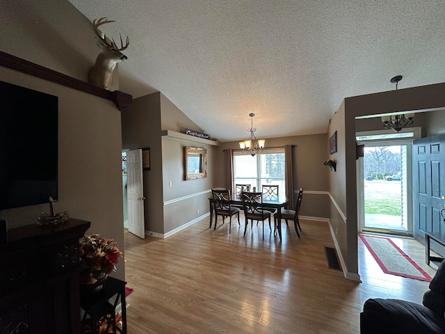 dining space with a healthy amount of sunlight, a textured ceiling, wood-type flooring, and a notable chandelier