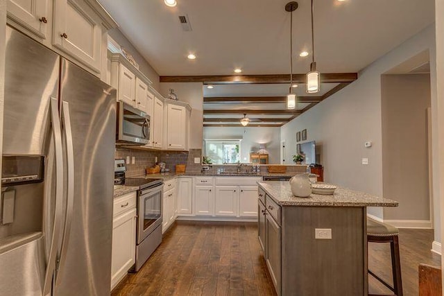 kitchen featuring decorative light fixtures, appliances with stainless steel finishes, a center island, beam ceiling, and a breakfast bar area