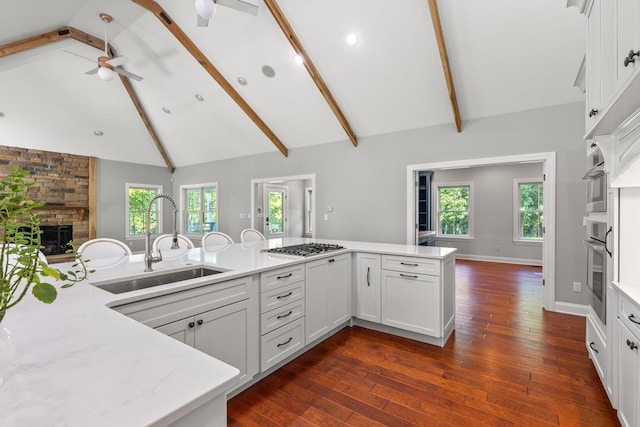 kitchen featuring beam ceiling, a sink, white cabinetry, stainless steel appliances, and a fireplace