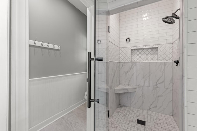 full bath featuring a wainscoted wall, toilet, and a shower stall