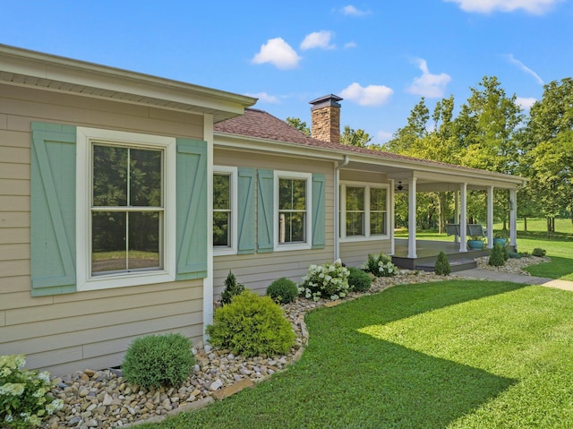 rear view of property featuring a lawn, a chimney, and roof with shingles