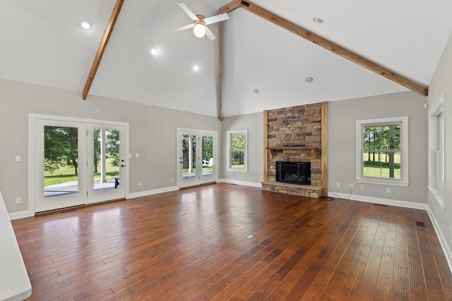 unfurnished living room with beamed ceiling, baseboards, a stone fireplace, and wood finished floors