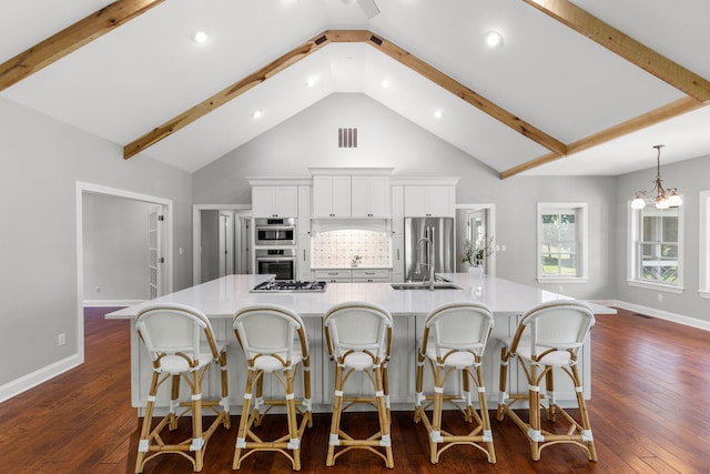 kitchen featuring a spacious island, dark wood finished floors, beamed ceiling, stainless steel appliances, and a sink