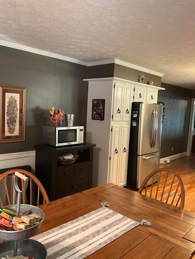 interior space featuring ornamental molding, white cabinets, stainless steel appliances, a textured ceiling, and light wood-type flooring