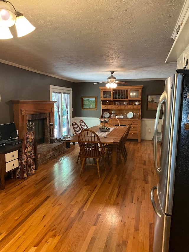 dining room featuring ceiling fan, crown molding, light hardwood / wood-style flooring, a fireplace, and a textured ceiling