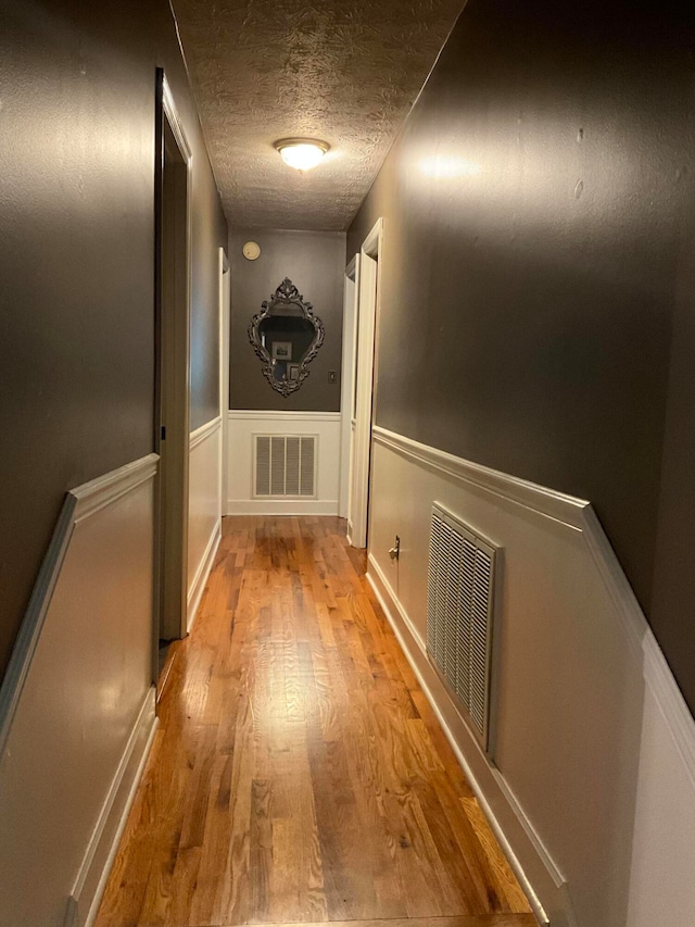 hallway with light hardwood / wood-style floors and a textured ceiling