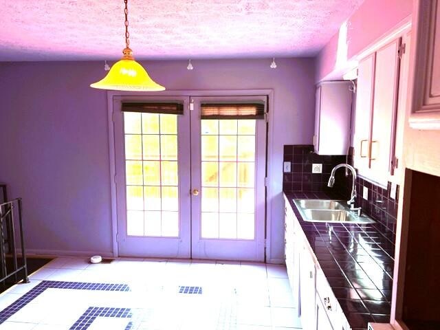 kitchen with tasteful backsplash, white cabinetry, sink, hanging light fixtures, and light tile flooring