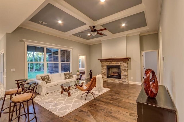 living room featuring dark wood-type flooring, ceiling fan, beam ceiling, coffered ceiling, and a stone fireplace