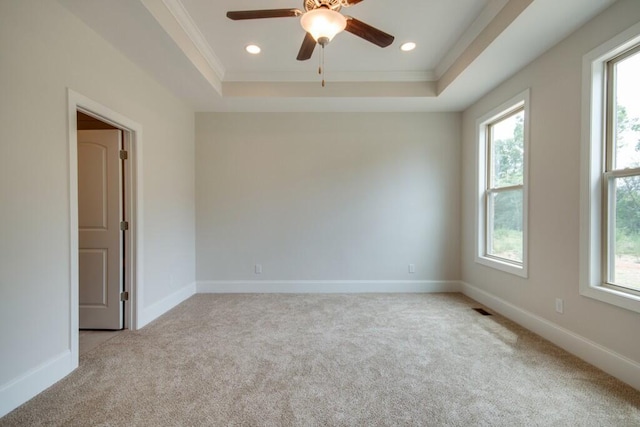 spare room with ceiling fan, ornamental molding, a tray ceiling, and light colored carpet