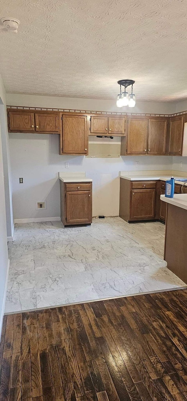 kitchen featuring light wood finished floors, baseboards, brown cabinetry, light countertops, and a textured ceiling