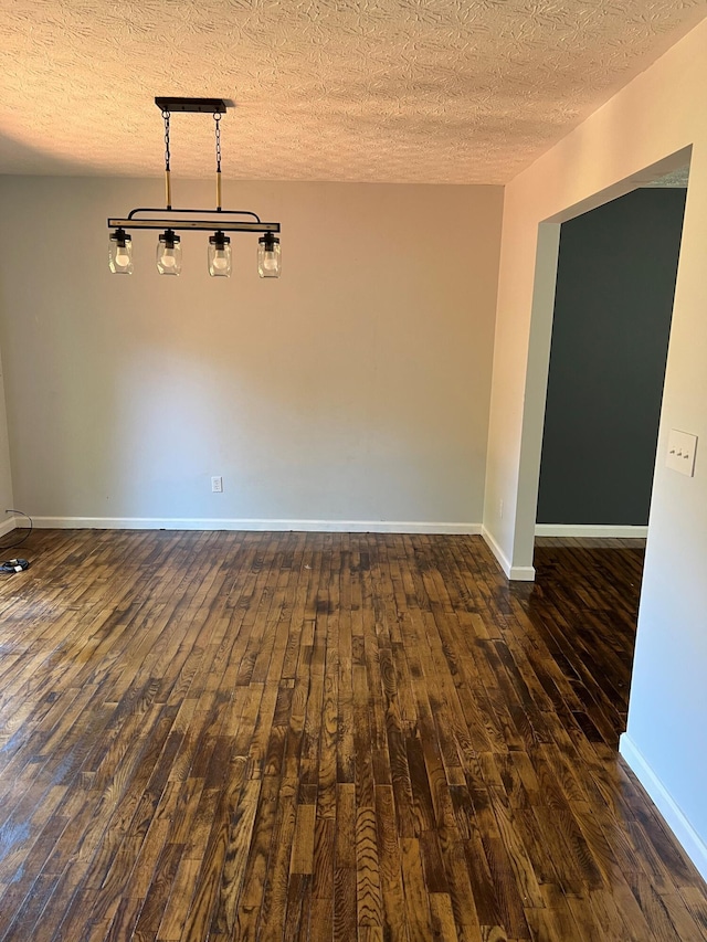 unfurnished room with dark wood-type flooring, a textured ceiling, and baseboards