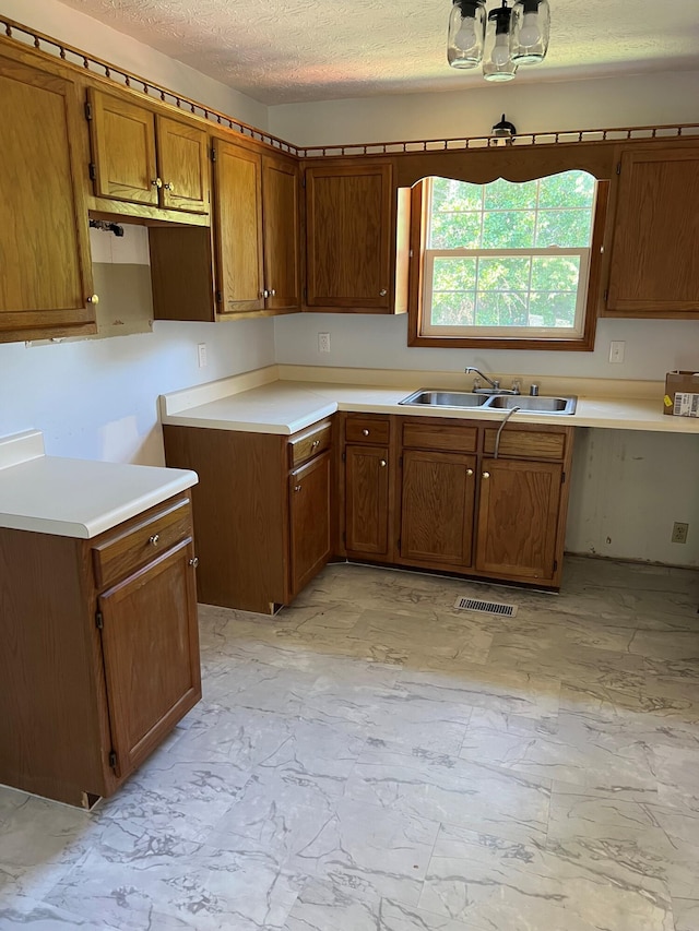 kitchen featuring marble finish floor, brown cabinets, visible vents, a sink, and a textured ceiling