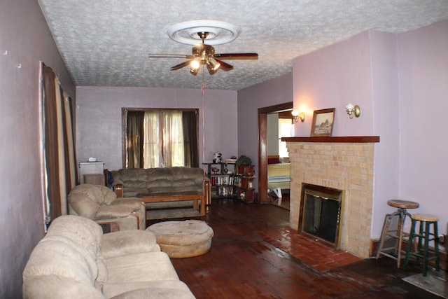 living room featuring ceiling fan, a brick fireplace, dark wood-type flooring, and a textured ceiling