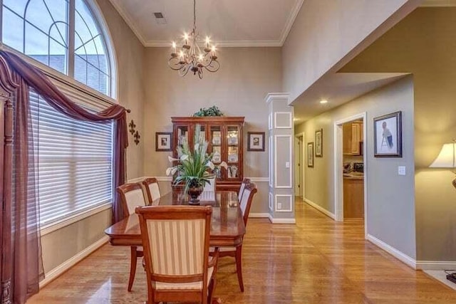 dining space with light hardwood / wood-style flooring, ornamental molding, an inviting chandelier, and decorative columns