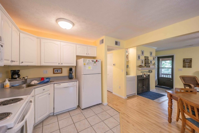 kitchen featuring white cabinets, light tile floors, a textured ceiling, white appliances, and sink