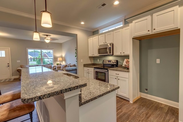 kitchen featuring an island with sink, pendant lighting, appliances with stainless steel finishes, dark stone countertops, and dark wood-type flooring