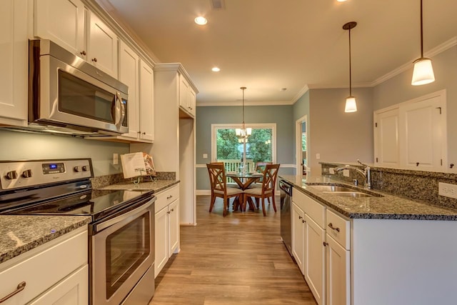 kitchen with dark stone countertops, stainless steel appliances, decorative light fixtures, and light wood-type flooring