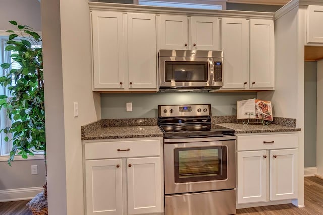 kitchen with white cabinets, dark stone countertops, stainless steel appliances, and light wood-type flooring