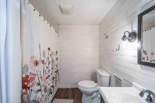 bathroom with toilet, wood-type flooring, wood walls, and vanity