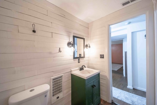 bathroom featuring wooden walls, toilet, vanity, and hardwood / wood-style flooring