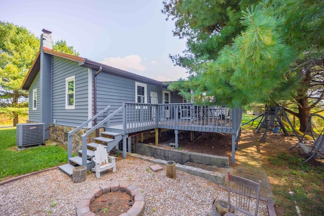 back of property with a deck, central air condition unit, a playground, and an outdoor fire pit