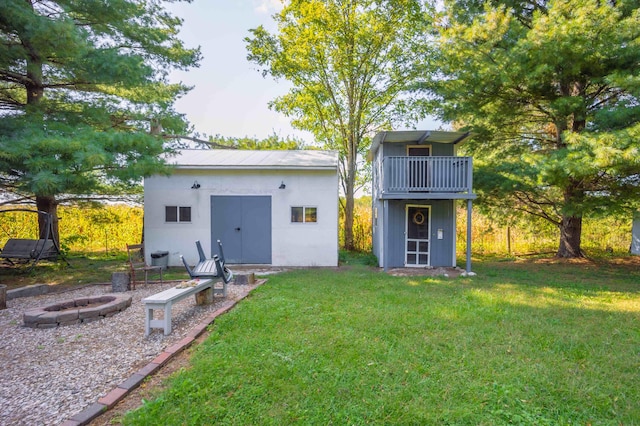 back of property featuring a balcony, a fire pit, an outdoor structure, and a lawn