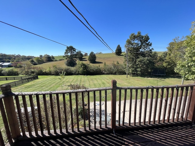 wooden deck with a trampoline, a yard, and a rural view