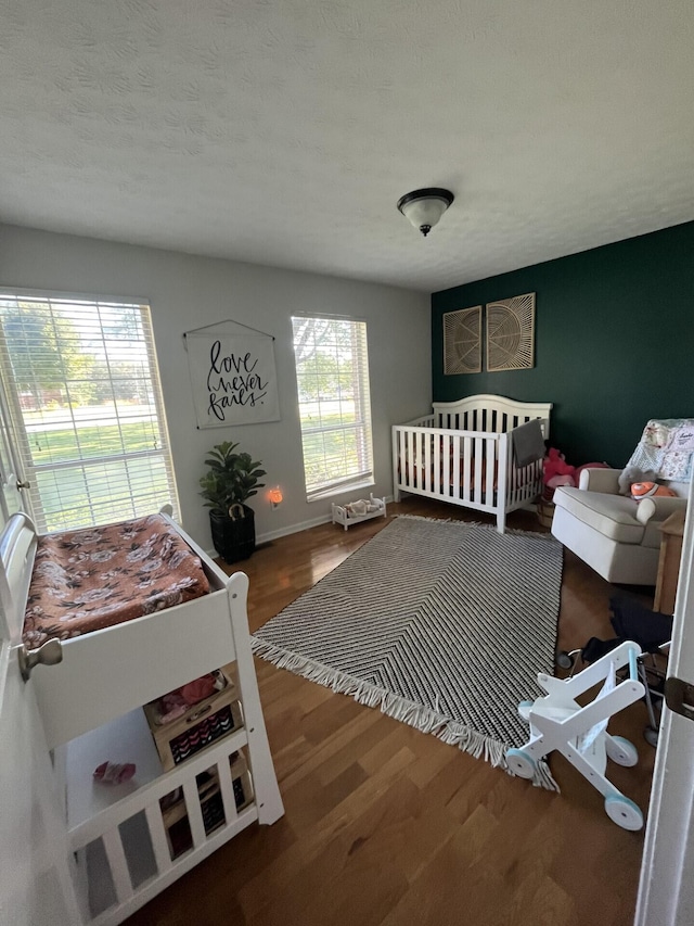 bedroom with a nursery area, hardwood / wood-style floors, and a textured ceiling