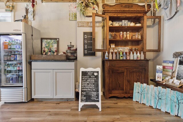 bar featuring light hardwood / wood-style floors, white cabinetry, and stainless steel refrigerator