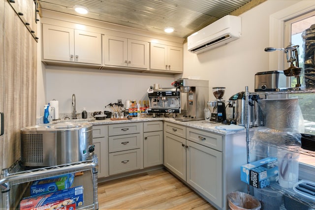 kitchen with a wall mounted air conditioner, gray cabinetry, sink, light hardwood / wood-style floors, and light stone counters