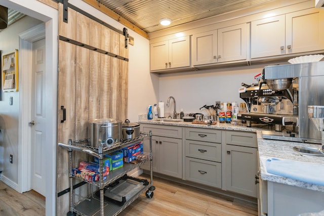 kitchen featuring light stone countertops, gray cabinetry, sink, a barn door, and light hardwood / wood-style flooring