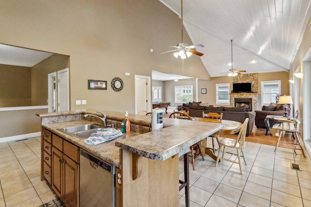 kitchen with sink, stainless steel dishwasher, an island with sink, a kitchen bar, and light tile patterned floors