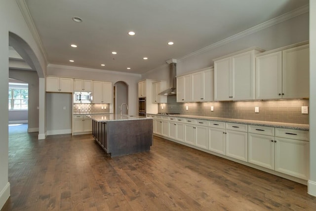 kitchen with stainless steel appliances, dark wood-type flooring, an island with sink, and wall chimney range hood