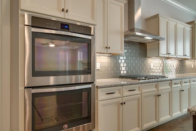 kitchen featuring appliances with stainless steel finishes, light stone countertops, backsplash, and wall chimney range hood