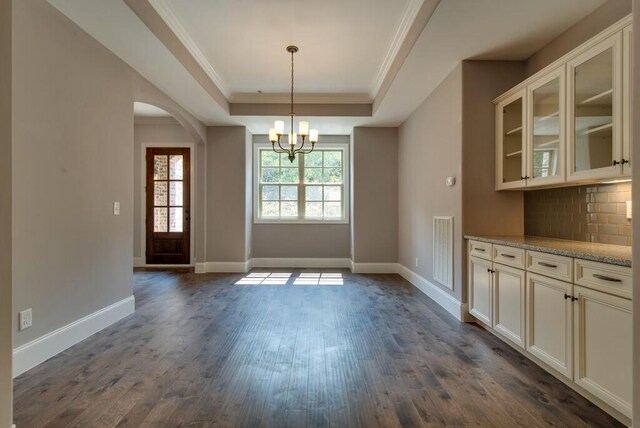 unfurnished dining area featuring crown molding, a chandelier, a tray ceiling, and dark hardwood / wood-style flooring