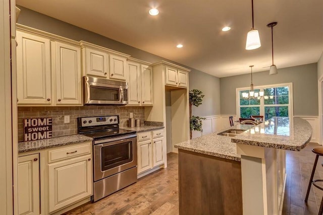 kitchen with an inviting chandelier, appliances with stainless steel finishes, light hardwood / wood-style floors, light stone counters, and pendant lighting