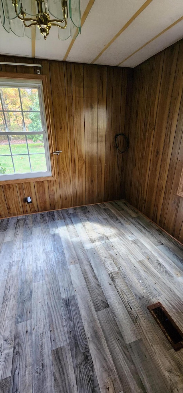 empty room with wood walls, dark hardwood / wood-style floors, and a chandelier