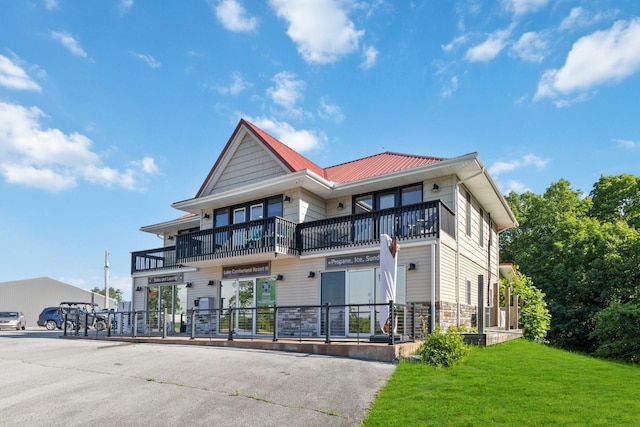 view of front of home with a front yard, a balcony, stone siding, and metal roof