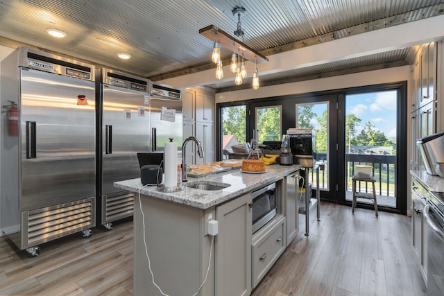 kitchen with sink, built in appliances, a center island with sink, white cabinets, and light hardwood / wood-style floors