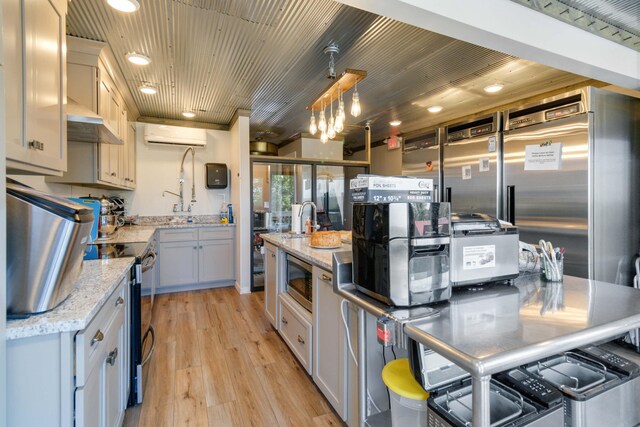 kitchen with a wall mounted air conditioner, light wood-type flooring, light stone counters, built in appliances, and hanging light fixtures