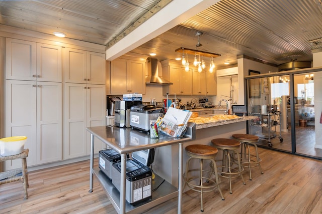 kitchen with light wood finished floors, wall chimney range hood, a breakfast bar, light stone counters, and wooden ceiling