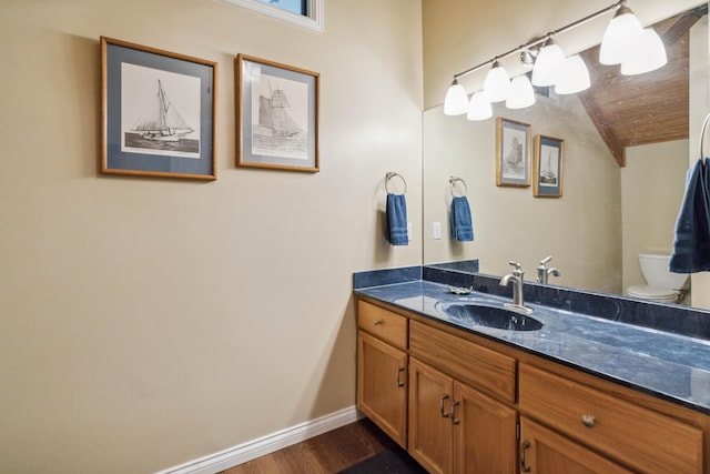 bathroom with baseboards, toilet, vaulted ceiling, wood finished floors, and vanity