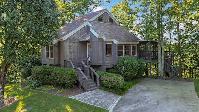 view of front facade with a front lawn, roof with shingles, stairs, and a sunroom